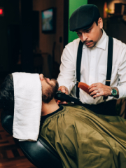 Detalhe das mãos do barbeiro utilizando uma navalha para fazer a barba do cliente.