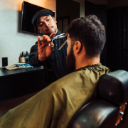 Barbeiro realizando corte de cabelo com tesoura em um cliente sentado.