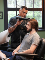 Barbeiro utilizando um secador profissional para modelar o cabelo do cliente.